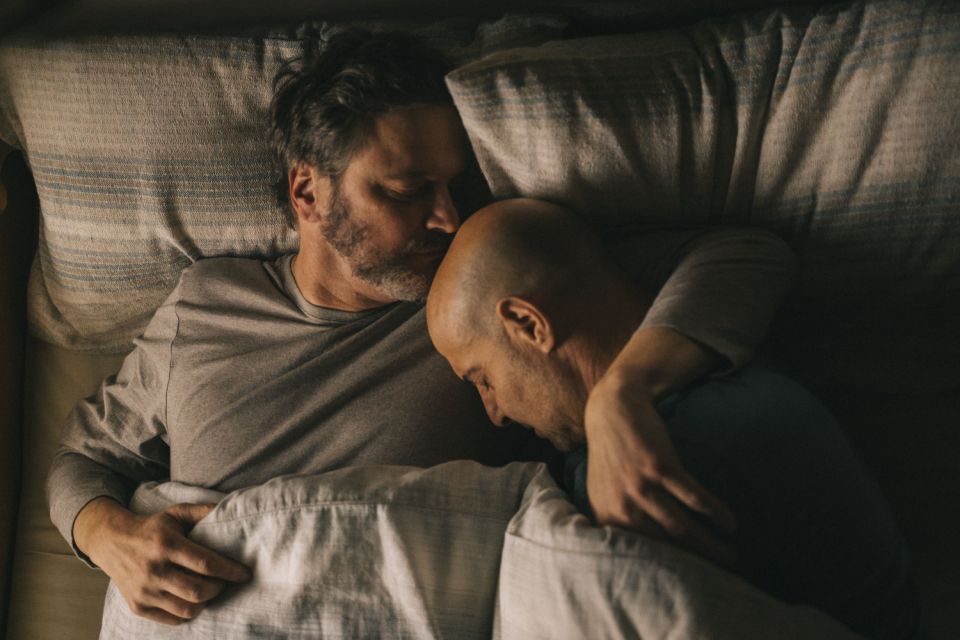 Gay couple and Stanley Tucci Harry MacQueen and Colin Firth share a tender embrace in bed in Supernova film.