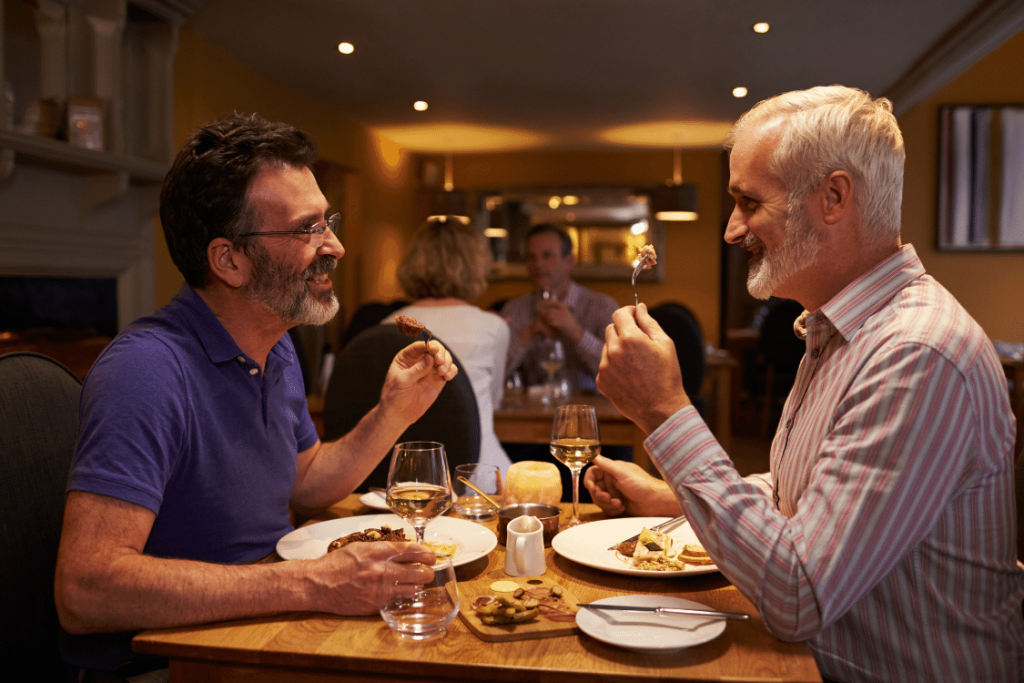 Gay male couple smiling at each other as they enjoy dinner out at a restaurant.