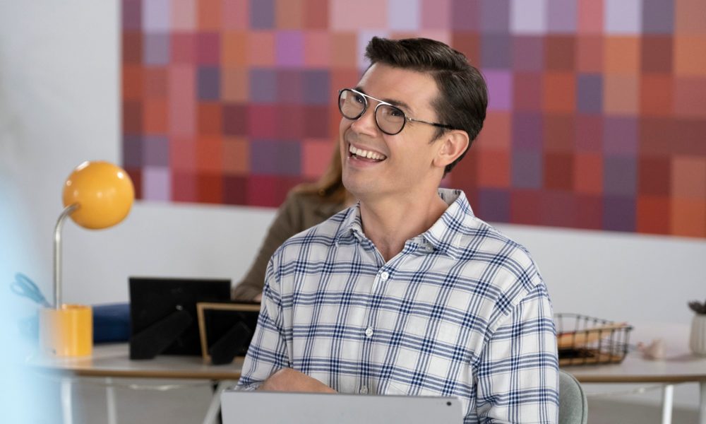 An image from SPECIAL season two showing Ryan O'Connell sitting at his work desk and smiling. 